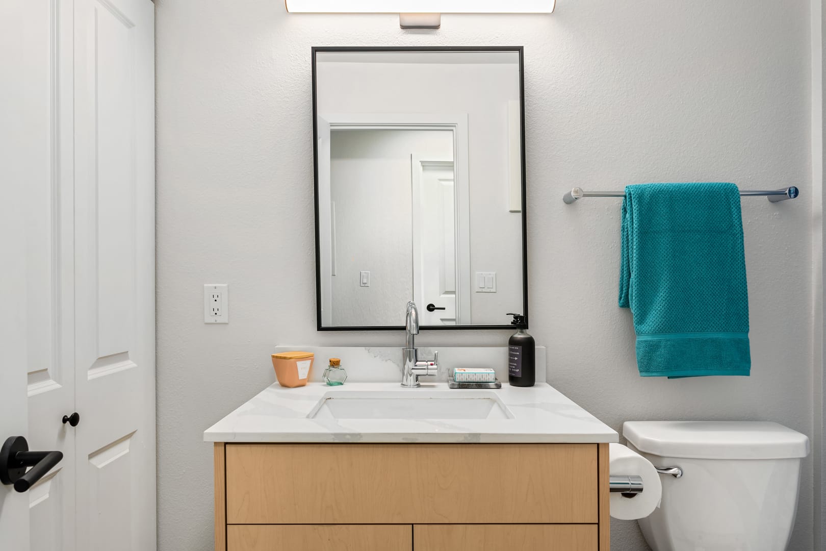 Bathroom with a modern single sink vanity, black trim mirror, and teal towel hanging from a rack